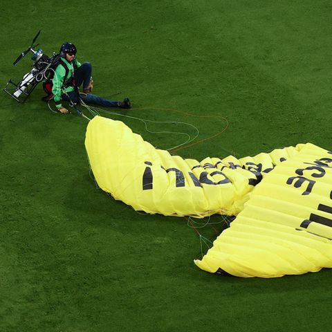 Ein Greenpeace-Aktivist sitzt mit einem gelben Fallschirm auf dem Fußballrasen in München