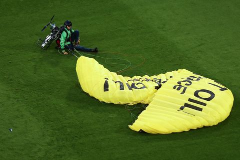 Ein Greenpeace-Aktivist sitzt mit einem gelben Fallschirm auf dem Fußballrasen in München