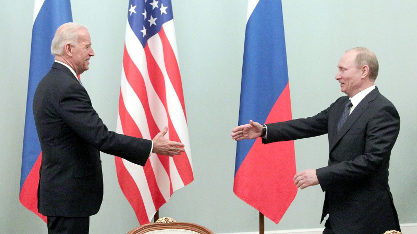 Treffen von Biden und Putin im Jahr 2011 Joe Biden und Wladimir Putin reichen sich die Hände vor den Flaggen von Russland und den USA