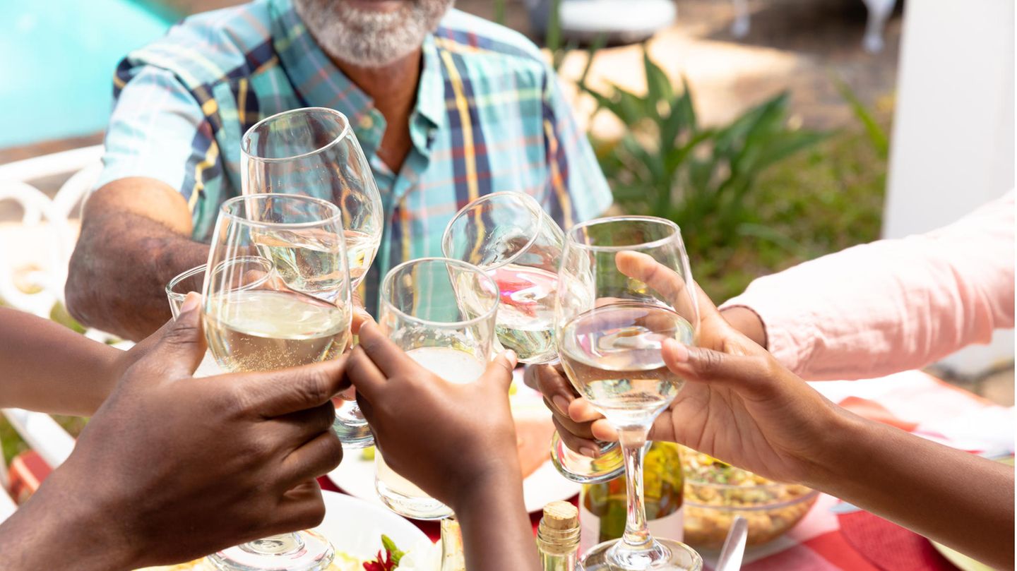 Mehrere Hände halten Wein- oder Wassergläser und stoßen über einem gedeckten Tisch an