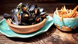 Moules frites  Zutaten: 5 große mehligkochende oder vorwiegend festkochende Kartoffeln, 2 kg küchenfertige frische Miesmuscheln, 4–6 Schalotten, 2 Knoblauchzehen, Olivenöl zum Anschwitzen, 400 ml trockener Weißwein, 1 TL Kräuter der Provence, 1 l Pflanzenöl, Salz  Zubereitung: Die Kartoffeln schälen, in dicke Stifte schneiden und beiseitestellen. Die Muscheln waschen, bereits geöffnete und angebrochene wegwerfen. Die Schalotten und den Knoblauch abziehen, fein hacken und in reichlich Olivenöl in einem Topf glasig anschwitzen. Mit dem Weißwein ablöschen und den Sud auf die Hälfte reduzieren. Dann die Muscheln und die Kräuter der Provence in den Topf geben. Alles gut umrühren und bei geschlossenem Deckel 10–15 Minuten kochen lassen. Ab und zu umrühren. Die im Anschluss an die Garzeit geschlossenen Muscheln aussortieren und wegwerfen. (Ungeöffnete Muscheln sind nicht zum Verzehr geeignet.) Die Kartoffelstifte in reichlich heißem Öl in einem Topf goldbraun frittieren. Dann mit einer Schöpfkelle aus dem Öl nehmen und auf Küchenpapier abtropfen lassen. Mit etwas Salz würzen. Die Muscheln mit dem Sud auf tiefen Tellern anrichten und mit den Pommes frites zusammen servieren