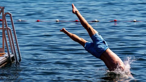 Ein junger Mann springt von einer Schwimmplattform aus in einen zum Schwimmen abgesperrten Bereich der Kieler Förde