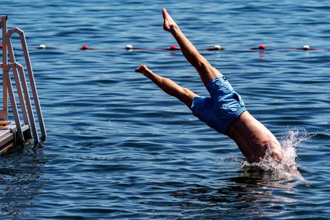 Ein junger Mann springt von einer Schwimmplattform aus in einen zum Schwimmen abgesperrten Bereich der Kieler Förde