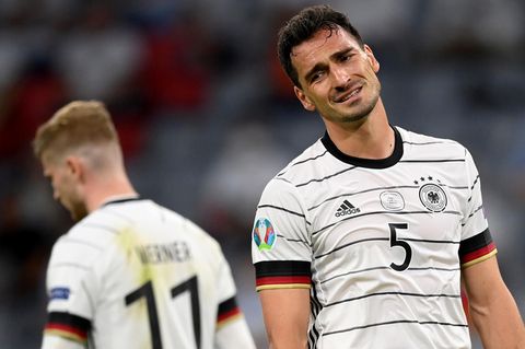 Ein weißer Mann mit kurzen, dunkelbraunen Locken steht im weißen DFB-Trikot im Stadion und lchelt gequält
