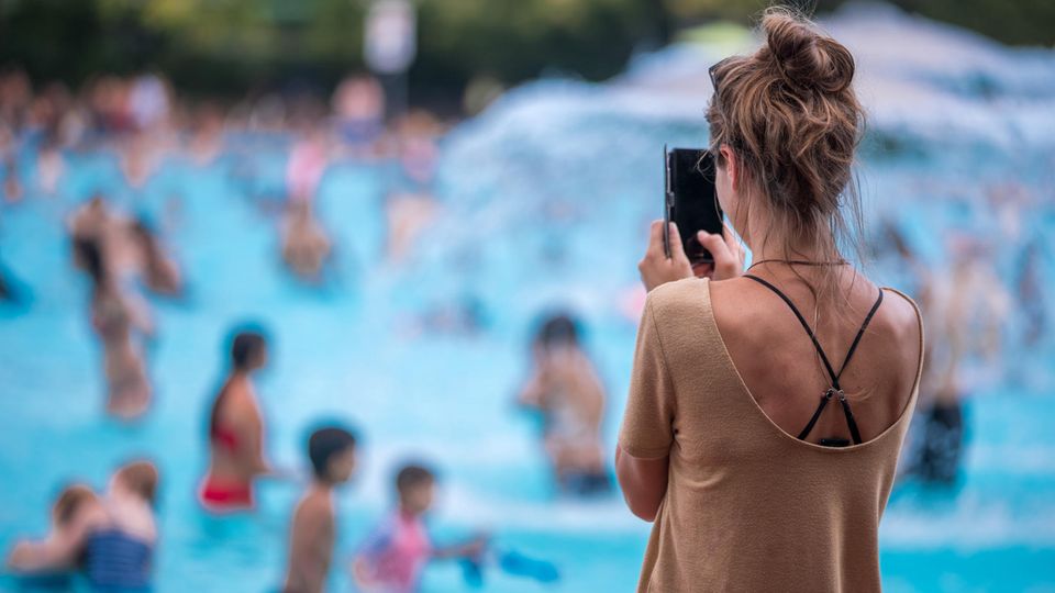 Eine junge Frau fotografiert mit ihrem Handy im Freibad