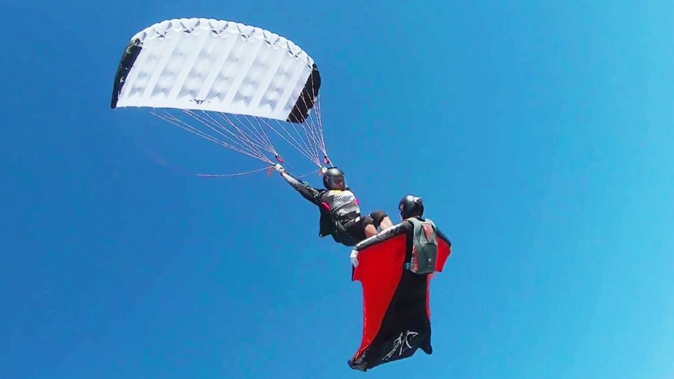 Fallschirmspringer gleitet wie auf einem Surfbrett auf der Brust einer Wingsuit-Pilotin