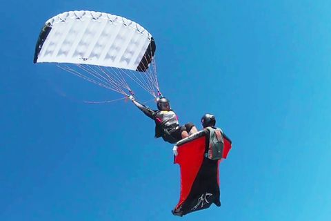 Fallschirmspringer gleitet wie auf einem Surfbrett auf der Brust einer Wingsuit-Pilotin