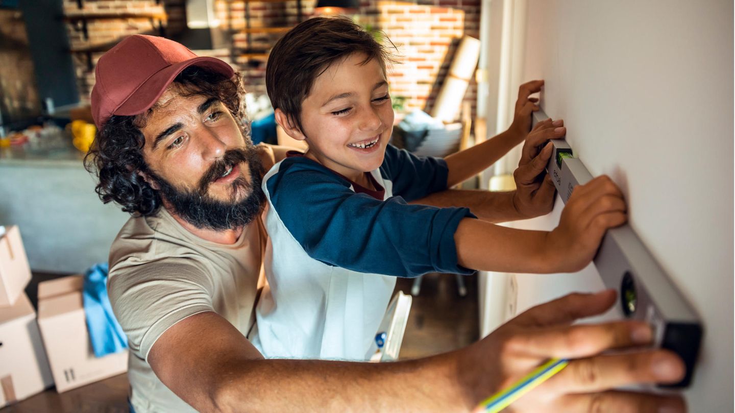 Vater und Sohn halten eine Wasserwaage an eine Wand