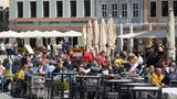 Wer hier genau hingeguckt hat, wird recht schnell den Hinweis auf Dresden auf dem kleinen, roten Schild entdeckt haben. An der Hausfassade im Hintergrund ist zudem der Schriftzug der Grill&Bar-Lokalität "Zum Schwan" zu erkennen. Kein Zweifel also, dass die Menschen hier auf dem Neumarkt an der berühmten Frauenkirche sitzen. Der ungefähre Ort bei Google Maps (hier noch mit einem anderen Lokal, da aus 2019).