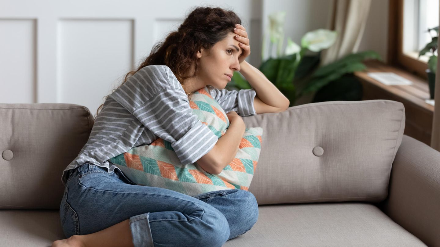 Long Covid Studie USA: Eine Frau sitzt auf einem Sofa und fasst sich an den Kopf