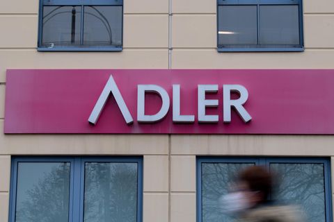 Eine Frau mit Mund-Nase-Bedeckung geht an einem Schild des Unternehmens Adler Modemärkte an einem Einkaufszentrum vorbei