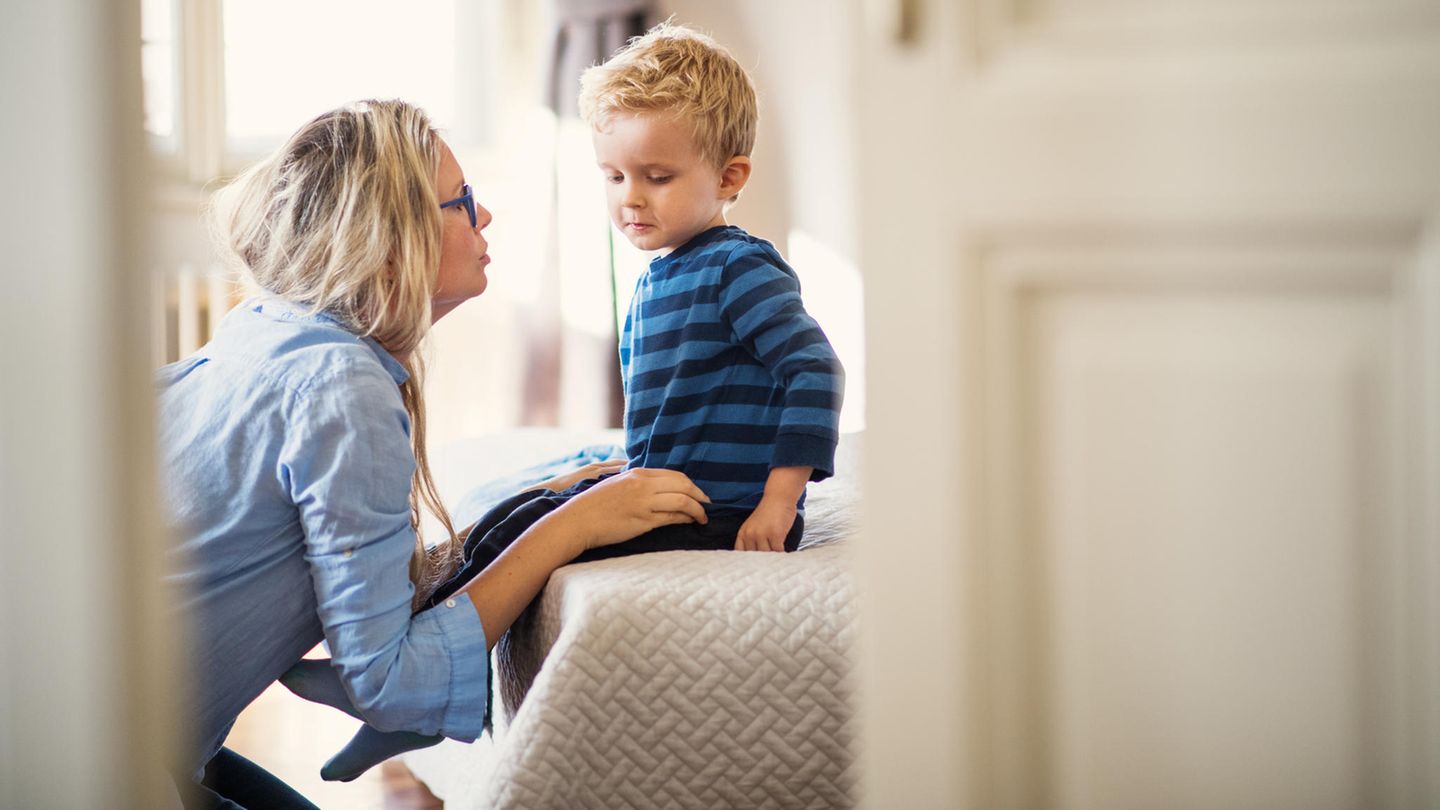 Eine junge Mutter im Gespräch mit ihrem kleinen Sohn in einem Schlafzimmer