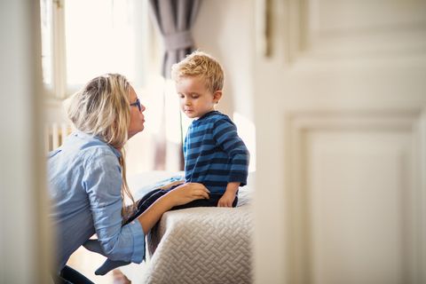 Eine junge Mutter im Gespräch mit ihrem kleinen Sohn in einem Schlafzimmer