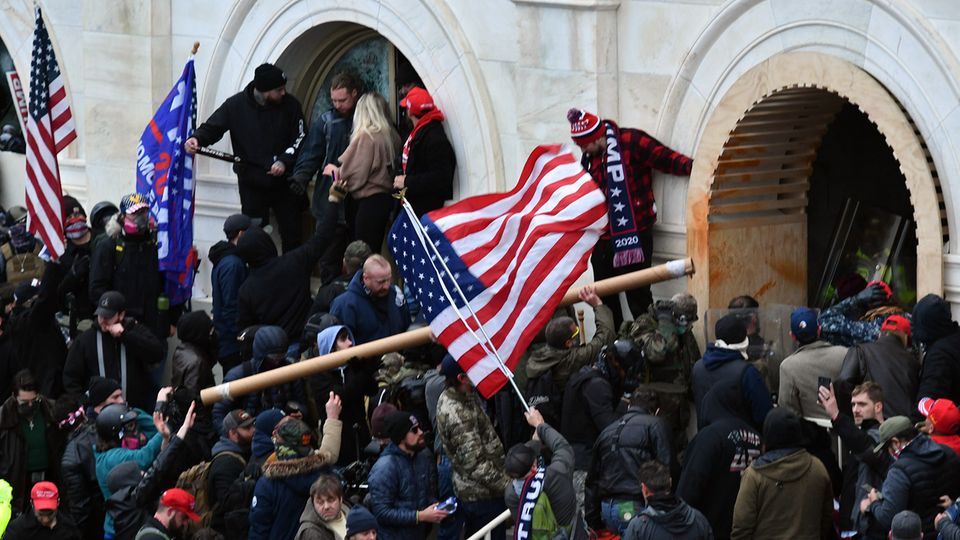Anhänger des damaligen US-Präsidenten Trump stürmen das US-Kapitolgebäude und schwingen eine USA-Flagge