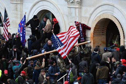 Anhänger des damaligen US-Präsidenten Trump stürmen das US-Kapitolgebäude und schwingen eine USA-Flagge