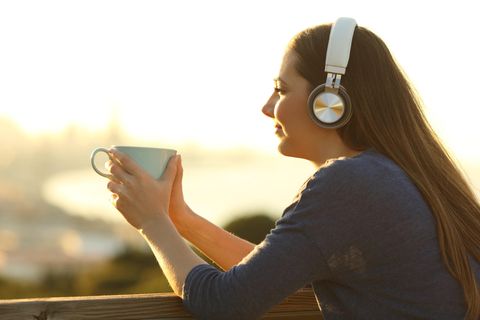 Frau hört Musik, guckt in die Sonne und trinkt aus einer Tasse
