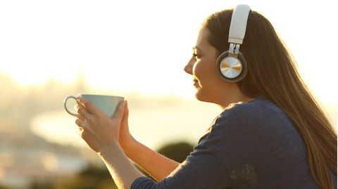 Frau hört Musik, guckt in die Sonne und trinkt aus einer Tasse