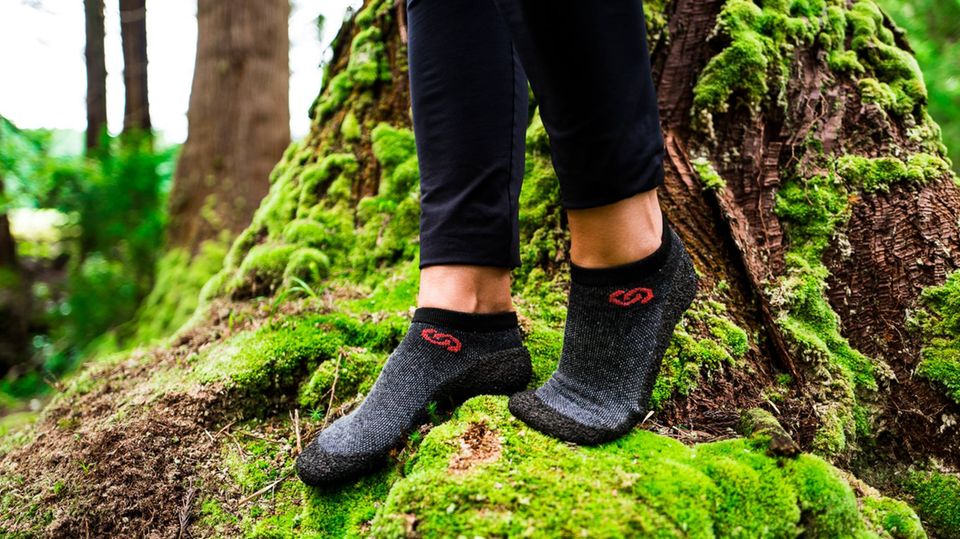 Sockenschuhe im Trend: Zwei Füße mit Sockenschuhen stehen auf vermoostem Baumstamm