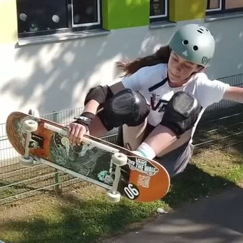 Eine junge weiße Teenagerin mit Helm und Ellenbogen- und Knieschonern springt mit einer Hand am Skateboard aus einer Halfpipe