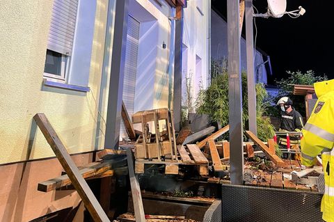 Rettungskräfte stehen neben den Trümmern eines Balkons aus Holz, der mit mehreren Menschen darauf eingestürzt ist.