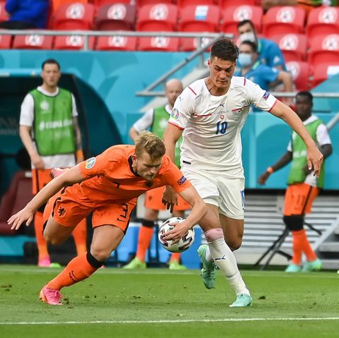 Ein Fußballer in orangem Dress greift im Fallen mit links nach dem Ball