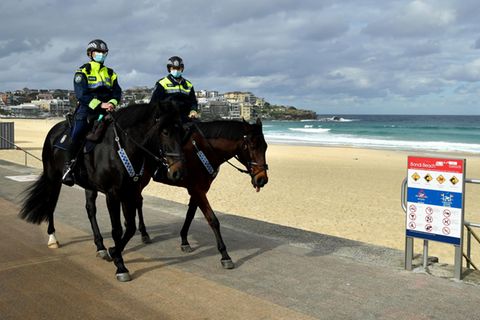 Zwei Polizisten auf Pferden reiten auf einer betonierten Strand-Promenade. Sie tragen Mund-Nasen-Schutz