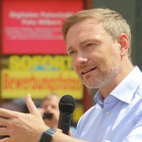 Christian Lindner mit Mikrofon in Erklärerpose vor rot-gelben Aufklebern