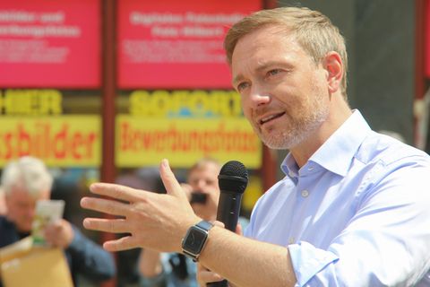 Christian Lindner mit Mikrofon in Erklärerpose vor rot-gelben Aufklebern