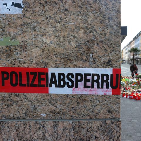 Blumen und Kerzen stehen in Würzburg vor einem Kaufhaus, im Vordergrund ist ein Absperrband der Polizei zu sehen