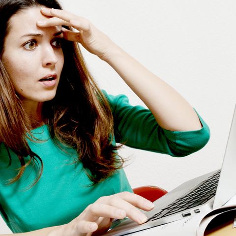 Eine Frau schaut auf ein Laptop und greift sich an den Kopf