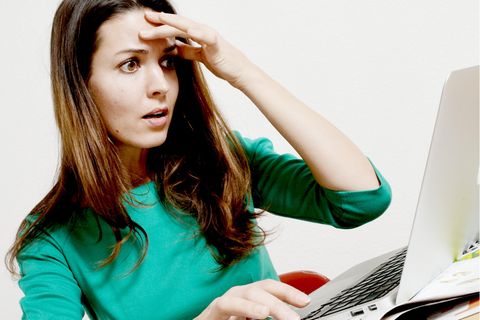 Eine Frau schaut auf ein Laptop und greift sich an den Kopf