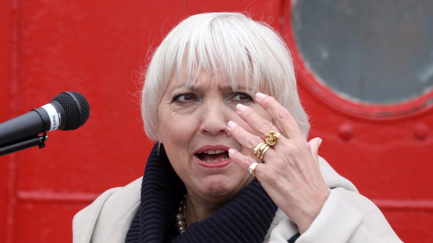 Claudia Roth mit erhobener Hand vor einem Mikrofon