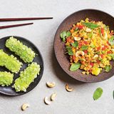 Ananasbratreis mit grünen Tofustäbchen      Zutaten: Ananas-Bratreis: 100 g Jasminreis, Salz, ¼ Ananas (ca. 100 g Fruchtfleisch), ½ rote Paprika (ca. 70 g), 1 mittelgroße Karotte (ca. 70 g), 2 Schalotten, 2 Knoblauchzehen, ½ gelbe Chilischote, 3 EL Bratöl (z.B. Sojaöl), 40 g TK-Erbsen, 1 EL Sojasauce, 1 EL »No-Fish-Sauce« (alternativ Sojasauce), 1 EL frisch gepresster Limettensaft, 1 TL vietnamesisches Currypulver (alternativ Madras-Currypulver), frisch gemahlener schwarzer Pfeffer      Tofustäbchen: 200 g Naturtofu, 4 EL Sojasauce, 2 EL frisch gepresster Limettensaft, ½ TL Zucker, ½ TL Chiliflocken, 50 g Reismehl, Salz, 40 g Tapiokastärke, 100 g grüner Reis (grüne Reisflocken), ca. 200 ml Bratöl (z.B. Sojaöl)      Außerdem: 1 Handvoll vietnamesische Kräuter (z.B. Koriandergrün, vietnamesischer Koriander und Minze), 1 Handvoll Cashewkerne, geröstet, 1 Portion klassische Dip-Sauce (Rezept Bild 2)      Zubereitung: Den Jasminreis am besten am Vorabend nach Packungsanleitung in Salzwasser zubereiten und über Nacht abkühlen lassen, so lässt sich der Reis am nächsten Tag am besser anbraten. Für die Tofustäbchen den Tofu quer in acht Stäbchen schneiden. In einer flachen Schale mit Sojasauce, Limettensaft, 4 EL Wasser, Zucker und Chiliflocken mindestens 30 Minuten unter Wenden marinieren. Inzwischen 30 g Reismehl mit 2 Prisen Salz in einer flachen Schale mischen. Das übrige Reismehl (20 g) mit Tapiokastärke und 100 ml kaltem Wasser verrühren, ebenfalls leicht salzen und in eine flache Schale füllen.  Den grünen Reis in einer dritten Schale bereitstellen. Die Tofustäbchen abtropfen lassen und im Reismehl, in der Stärkemischung und schließlich in den grünen Reisflocken wenden und 30 Minuten kalt stellen. Inzwischen für den Reis die Ananas schälen, den Mittelteil entfernen und das Fruchtfleisch 1–2 cm groß würfeln. Die Paprika putzen und 1 cm groß würfeln. Die Karotte schälen und ebenfalls 1 cm groß würfeln. Schalotten und Knoblauch abziehen und fein würfeln. Die Chilischote putzen und in Ringe schneiden. 1 EL des Bratöls in einer großen Pfanne erhitzen. Schalotten, Knoblauch, Chili, Paprika und Karotte darin bei hoher Temperatur unter Rühren etwa 3 Minuten braten. Ananas und Erbsen zugeben und 3 Minuten mitbraten. Alles auf einen Teller geben. Den Backofen auf 100°C Ober- und Unterhitze vorheizen.  Das übrige Öl (2 EL) in der Pfanne erhitzen und den Reis darin unter Rühren etwa 3 Minuten anbraten. Das Gemüse unter den Reis mischen. Sojasauce, »No-Fish-Sauce«, Limettensaft, Currypulver und Pfeffer verrühren und zum Reis geben. Unter Rühren weitere 2 Minuten garen, dann im Ofen warm halten. Für den Tofu das Bratöl in einem Wok oder einer Pfanne mit hohem Rand erhitzen. Die Tofustäbchen darin portionsweise unter gelegentlichem Wenden 3–5 Minuten braten und abtropfen lassen. Den Bratreis auf zwei Teller verteilen, mit Kräutern und Cashewkernen garnieren und mit Tofustäbchen servieren. Auf Wunsch die Dip-Sauce dazu reichen.