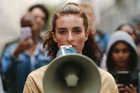 Eine junge Frau der Generation Z steht mit einem Megaphon auf der Straße.