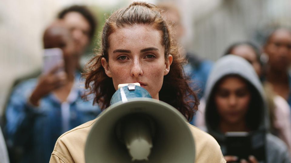 Eine junge Frau der Generation Z steht mit einem Megaphon auf der Straße.