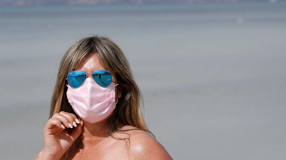 Eine Mallorca-Urlauberin trägt eine medizinische Maske, während sie die Sonne am Strand von El Arenal genießt.