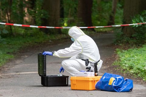 Ein Mitarbeiter der Spurensicherung trägt einen weißen Schutzanzug und nimmt Material aus einem Koffer