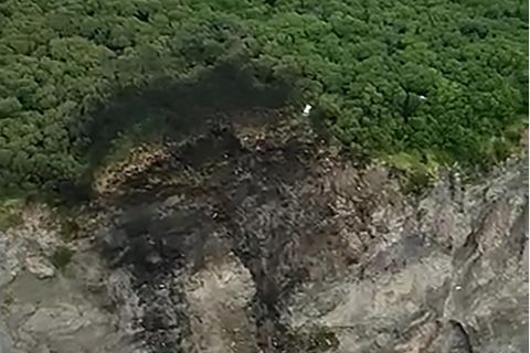 An der Kante einer bewaldeten Klippe sind Brandspuren und Schleifspuren die Felsen hinab zu sehen