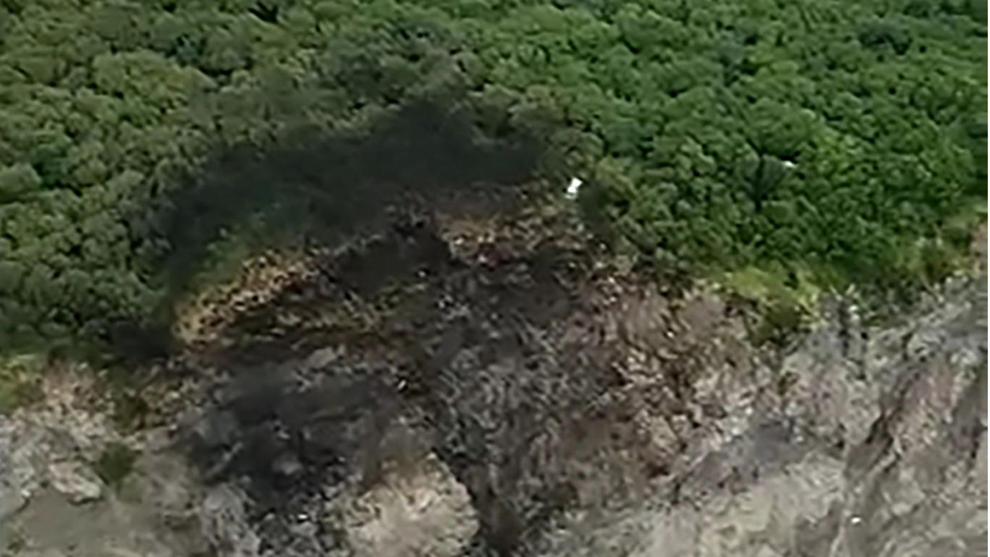 An der Kante einer bewaldeten Klippe sind Brandspuren und Schleifspuren die Felsen hinab zu sehen