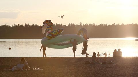 Badegäste tragen ein Schwimmreifen in Form eines Einhorns über den Strand während die Sonne untergeht