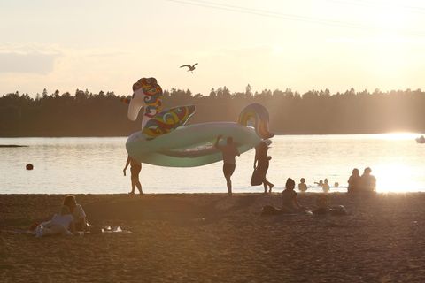 Badegäste tragen ein Schwimmreifen in Form eines Einhorns über den Strand während die Sonne untergeht