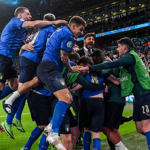 Eine Gruppe Fußballer in blauem Dress jubelt gemeinsam in einer Traube mit ihrem Trainer im Anzug
