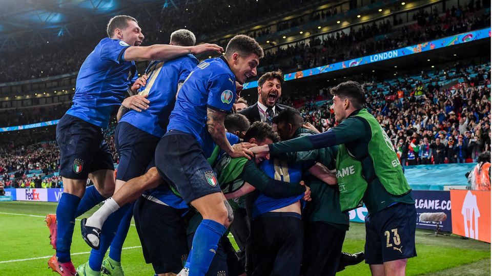 Eine Gruppe Fußballer in blauem Dress jubelt gemeinsam in einer Traube mit ihrem Trainer im Anzug