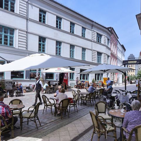 Passanten genießen in einem Straßencafé in Schwerin das sommerlichem Wetter