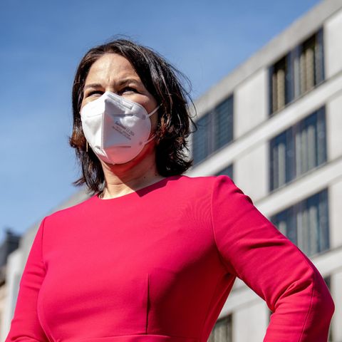 Eine weiße Frau mit schulterlangen, braunen Haaren steht mit FFP2-Maske unter freiem Himmel in der Sonne.