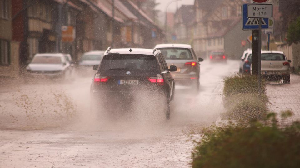 Starkregen im Sommer Unwetter im Sommer in Deutschland: Autos fahren durch eine unterspülte Straße.