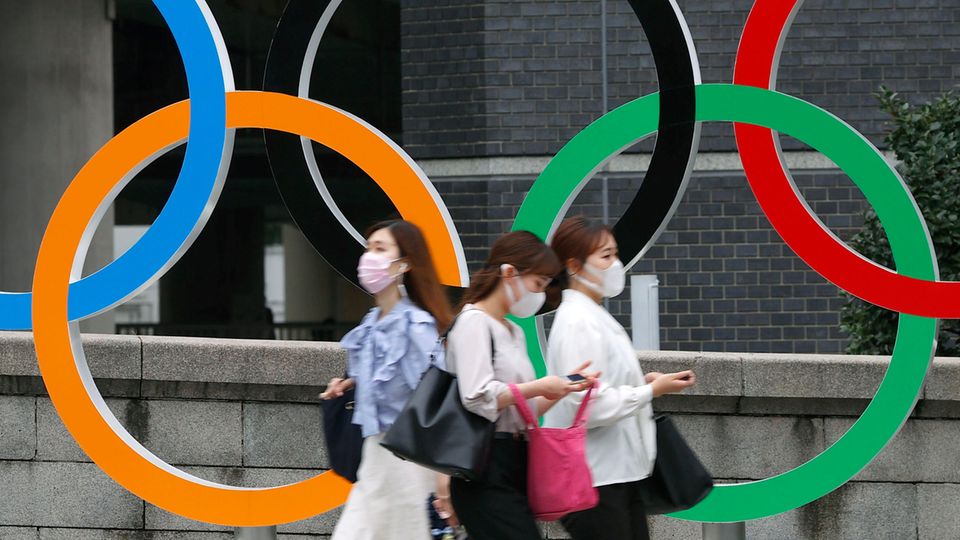 Menschen mit Gesichtsmasken gehen an der Statue der Olympischen Ringe in Tokio (Japan) vorbei