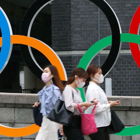 Menschen mit Gesichtsmasken gehen an der Statue der Olympischen Ringe in Tokio (Japan) vorbei