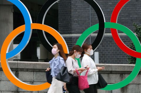 Menschen mit Gesichtsmasken gehen an der Statue der Olympischen Ringe in Tokio (Japan) vorbei