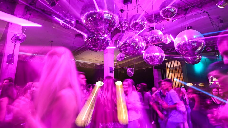 In a pink-lit club, young people dance under several disco balls